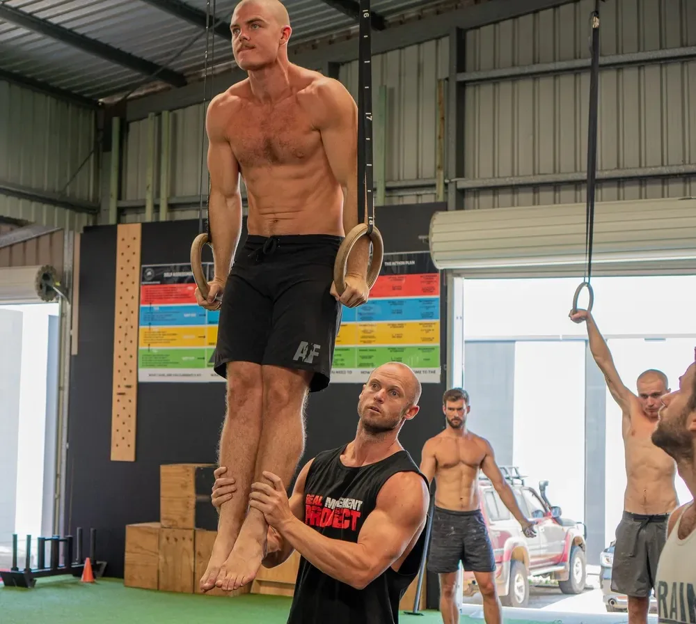 Coach spotting an athlete holding a ring support during a group strength session